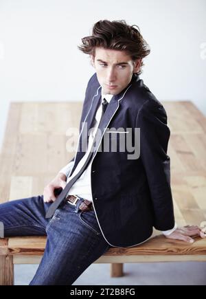 Fashion, table and attractive man in a studio with formal, classy and elegant outfit for aesthetic. Handsome, suit and serious young male model with Stock Photo