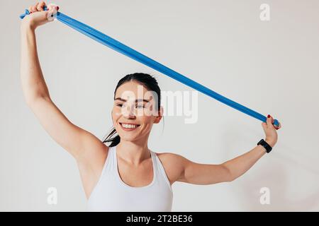 Young smiling woman with resistance band stretching her hands against the white backdrop Stock Photo