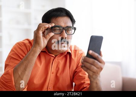 Mature Indian Man In Eyeglasses Looking At Smartphone Stock Photo