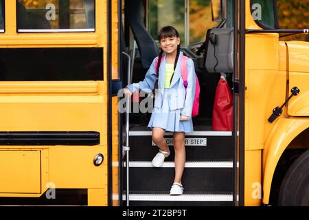 Smiling preteen asian girl getting of the yellow school bus Stock Photo