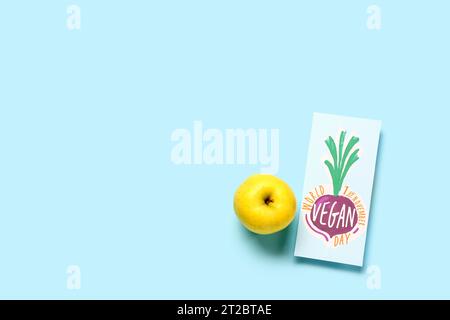 Card with text WORLD VEGAN DAY and apple on blue background Stock Photo