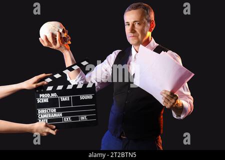 Mature actor with skull reading script on dark background Stock Photo