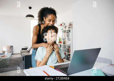 Cheerful woman helping daughter doing homework. Happy mother assisting her daughter with school homework in living room. Stock Photo