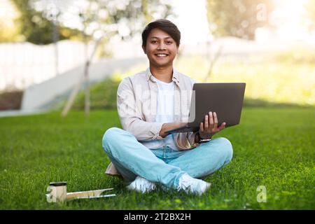 Handsome young asian guy working on laptop at park Stock Photo