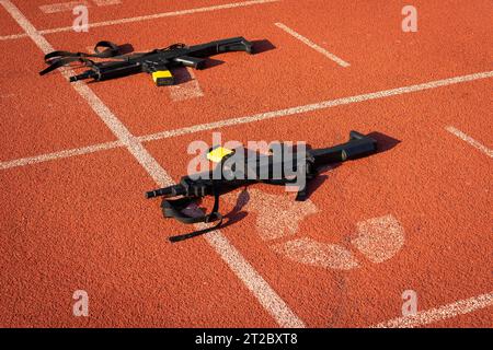 Black practice weapons on the dotted starting line of an orange running track Stock Photo