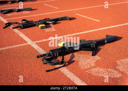 Black practice weapons on the dotted starting line of an orange running track Stock Photo