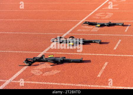 Black practice weapons on the dotted starting line of an orange running track Stock Photo