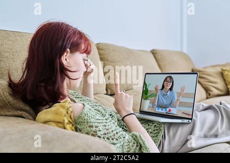 Online therapy, young female lying at home having video conference with psychologist Stock Photo