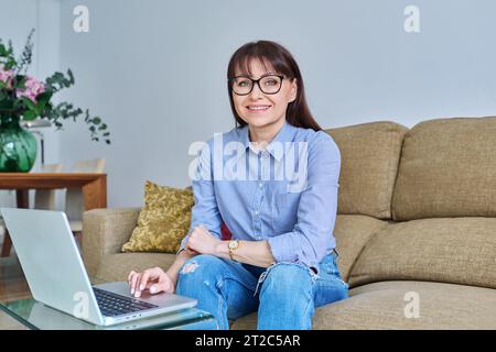 Portrait of middle-aged woman with laptop on sofa in living room Stock Photo