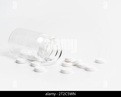 White pills scattered near opened glass bottle on white background. Concept of medical treatment with medication, vitamins or supplements in capsules Stock Photo