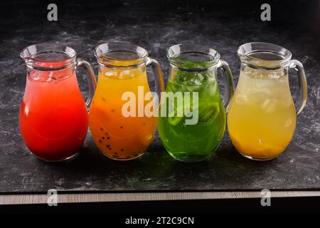 four lemonades with lemon, kiwi, apple, cucumber, rosemary and mint in glass bottles highlighted on a black background. Summer cold drink and soft dri Stock Photo