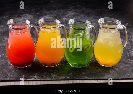 four lemonades with lemon, kiwi, apple, cucumber, rosemary and mint in glass bottles highlighted on a black background. Summer cold drink and soft dri Stock Photo