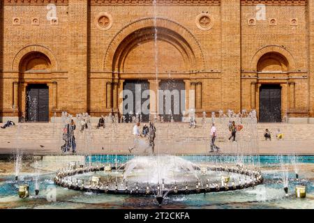 Medellin, Colombia - January 10, 2023: People, seen through the water jets of a fountain, walk in front of the Medellin cathedral Stock Photo