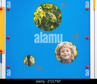 A little boy looks through a hole in a board Stock Photo