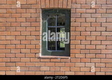 a small window with metal bars and cobwebs on a clay brick wall Stock Photo