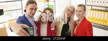Man holds smartphone taking selfie with female colleagues Stock Photo