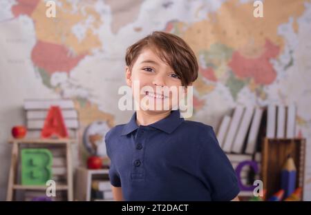 A young student is seated at his desk in a classroom setting, smiling cheerfully at the camera Stock Photo