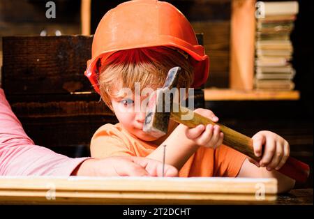 Funny little repairman with hammer. Kids construction worker. Child use a hammer to nail. Stock Photo