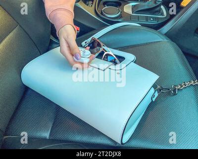 a girl with a pink manicure holds headphones without wires in her hands. flatley. bag and glasses in a car with leather seats. trendy and stylish look Stock Photo