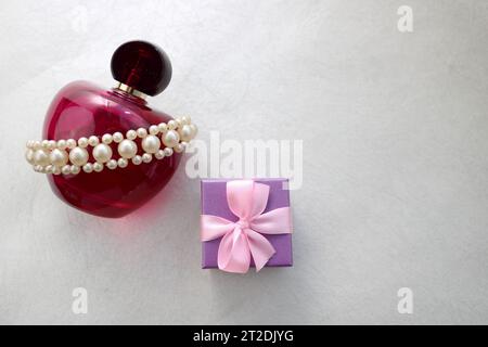 Pink beautiful glass transparent bottle of female perfume decorated with white precious pearls and blue small gift box and place for a simple text on Stock Photo