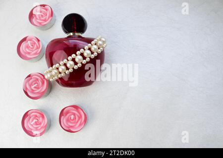 Violet beautiful glass transparent bottle of female perfume decorated with white dragon gems and pink paraffin candles in the shape of a rose and plac Stock Photo