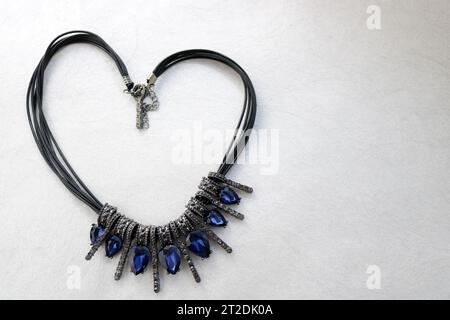 Heart made of female jewelry, necklaces with blue gems, diamonds, diamonds in the shape of a heart on a light gray background. Stock Photo