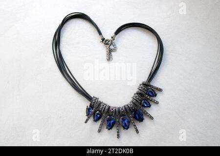 Heart made of female jewelry, necklaces with black threads, blue jewels, diamonds, diamonds in the shape of a heart on a light gray background. Stock Photo