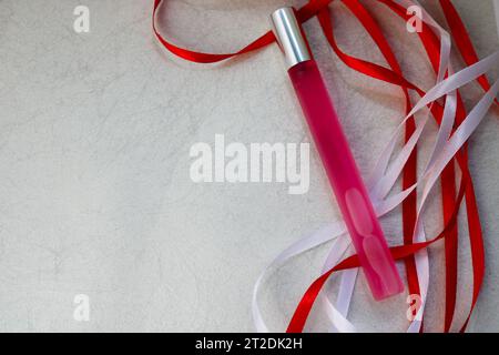 Texture with a pink matte thin long cylindrical perfume bottle, cologne with red and white beautiful festive ribbons made of artificial fabric on a li Stock Photo