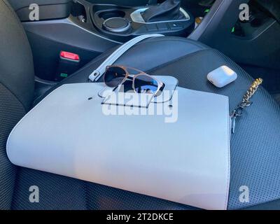 White women's beautiful fashionable leather bag and sunglasses with wireless headphones lie on the leather armchair of a good expensive car. Stock Photo