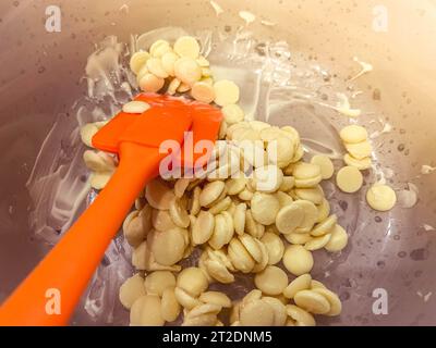 Melted hot white yummy sweet little round chocolate callets made from Belgian milk chocolate for tempering and making homemade sweet desserts and garn Stock Photo