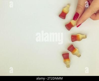 marmalade dessert. gummies in the form of a bottle with black lemonade. appetizing figurine, a girl with red nails holding a candy. semicircular candy Stock Photo