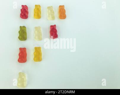 Big triangle ladder made of beautiful sweet delicious multicolored chewy bears juicy fruit gummy candies on a white background. Stock Photo