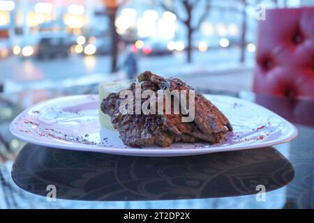 Fried meat, pork, beef on a white plate on a table in a cafe, restaurant in the evening. Stock Photo