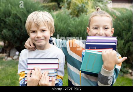 Two boy friends stand next to each other and hold stacks of books in front of them Stock Photo