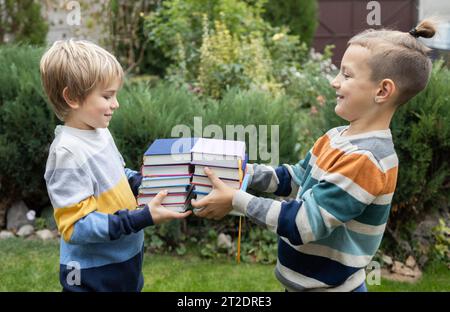 Two boy friends stand opposite each other and hold stacks of books in front of them Stock Photo