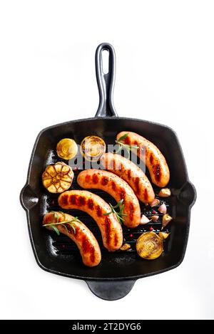 Grilled sausages with garlic and herbs on cast iron grill pan isolated on white background,  top view. Roasted homemade german wurst sausages. Stock Photo