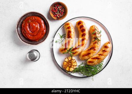 Grilled sausages with tomato sauce and herbs on white background, top view, copy space. Roasted homemade wurst sausages on plate. Stock Photo