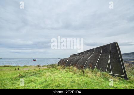 Former herring fishing boat, now upturned and used as a storage shed on the shore of the Holy Island of Lindisfarne, Northumberland, England. Stock Photo