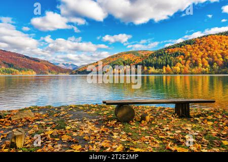 mountainous autumn landscape with lake. nature background with trees on the shore in fall colors. warm sunny weather with fluffy clouds on the sky Stock Photo