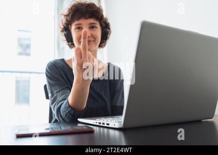 teenage girl shows middle finger while sitting in front computer Stock Photo