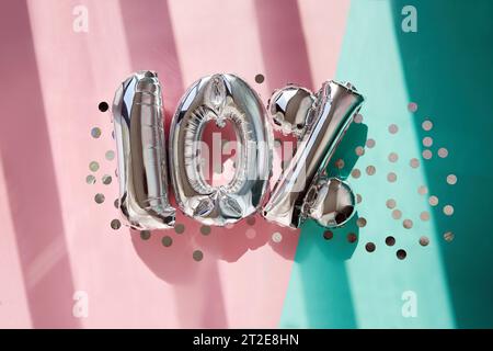 Silver numbers 10 ten percent balloons among confetti in sunlight on pink turquoise background celebration party. Greetings and congratulation Stock Photo