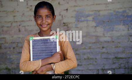 Portrait of happy cute little indian girl holding blank slate, Adorable elementary kid showing black board. child education concept. rural india. Stock Photo