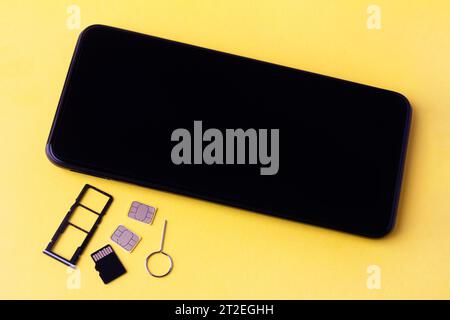 smartphone and open slots for nano SIM cards, two nano SIM cards, micro SD drive and metal key on yellow background Stock Photo