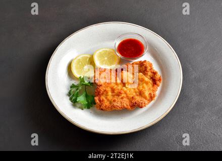 Schnitzel with lemon and leaves of parsley on white plate over brown stone background. Close up view Stock Photo