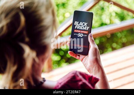 Black Friday shopping ad on a mobile phone screen. The woman holds a smartphone in her hand. Stock Photo