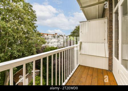 a balcony with wooden flooring and white railings on the side of a house, surrounded by lush green trees Stock Photo