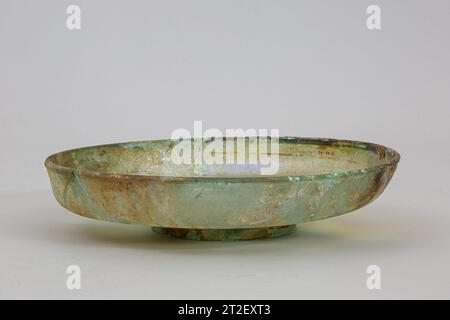 Glass dish Roman 3rd–4th century CE Translucent blue green.Rounded, thickened vertical rim, with slight outward lip; convex side to body, tapering downwards then curving sharply in to slightly pushed-in, sloping outer section of bottom; solid foot ring with rounded edge; inner section of bottom slightly concave.Broken and repaired on one side, with one small hole; some pinprick bubbles; dulling, pitting, brilliant iridescence, and patches of brownish weathering and encrustation. View more. Glass dish. Roman. 3rd–4th century CE. Glass; blown. Late Imperial. Glass Stock Photo