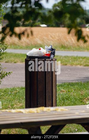 Public trash can in a park filled with overflowing trash Stock Photo