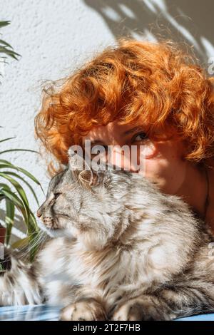 Portrait red-haired teenage girl and fluffy cat in sun Stock Photo