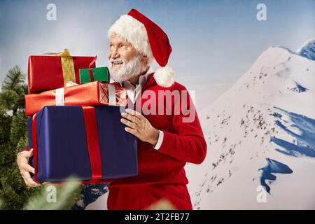 handsome man in Santa costume with presents in hands smiling and looking away, winter concept Stock Photo